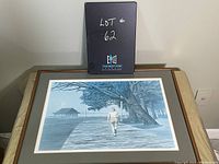 Framed Andy Donato print showing a person walking on a boardwalk by water and trees, shot from front with table and wall background