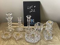 Set of nine assorted clear glass candle holders displayed on a table, showing various styles including tall taper candle holders and shorter tealight holders.