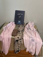 Front view of the gloves and three scarves laid out on a surface with a lot number sign behind.