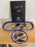 Set of two handmade glass plates, one round and one oval, showing leaf motif and textured clear glass with blue rim.