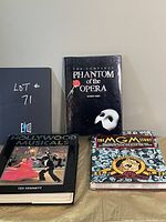 Three coffee table books displayed upright: The Complete Phantom of the Opera (center), Hollywood Musicals (left), and The MGM Story (right).