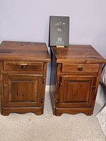 Front view of two matching vintage pine night tables with drawer and cupboard door on a carpeted floor.