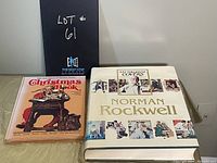 Photo of two hardcover books, 'Norman Rockwell 332 Magazine Covers' and 'The Saturday Evening Post Christmas Book', placed side by side on a neutral surface.