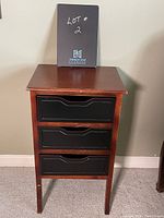 Front view of the three drawer occasional table showing reddish-brown wood frame and black drawer fronts with cutout handles.