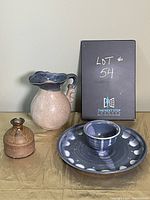 Three pottery items: beige and blue pitcher, blue chip and dip bowl with central dip cup, and small brown vase arranged on beige surface.