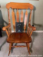 Front view of wooden rocking chair showing slatted back, curved arms, and carved legs in a medium wood finish