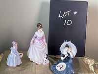 Trio of Royal Doulton figurines on display with lot number board behind