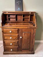 Front view of roll-top secretary desk with roll-top open showing internal cubbies and slots, 4 drawers on left, one cabinet door right with white knobs.