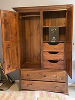 Open armoire showing left hanging compartment with rod and right interior drawers and shelf