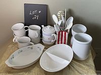 Photo showing six white ceramic mugs, floral sugar bowl, two serving plates, utensil holder with white serving spoons and ladle, white jar and small bowls.