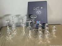 Photo showing six clear glass wine glasses and nine clear glass shot glasses arranged on a surface with box labeled 'Lot #53'