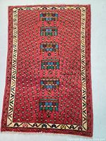 Full view of rectangular hand knotted Persian Mir wool rug with red field and multi medallion central column.