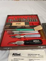 Top view of open Allied precision cutting tool set displaying various blades, knife handles, sanding block, and wedges in red tray insert inside case.