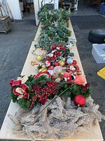 Top view of the long table covered with multiple green and silver artificial garlands, various Christmas ornaments, and strands of lights spread out for display.