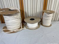 Three spools of white cotton piping cord of different sizes laid out for display.