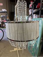 Full view of the chandelier showing fabric shade, central rod, and hanging crystal strands.