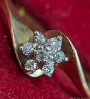 Close-up photo of 10K gold ring with floral diamond cluster on red background.