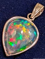 Front view of teardrop enhanced black opal pendant in 14K gold bezel setting on dark background showing vibrant multi-color play-of-color within the opal.