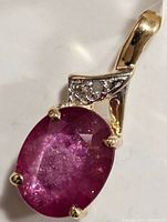 Close-up image of the pendant showing the oval glass-filled ruby and diamonds set in 14K gold.