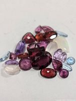 Close-up photo displaying a variety of small faceted genuine gemstones in multiple colors laid on a white surface.