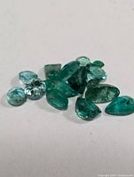 Close-up of loose emerald gemstones showing their shapes and natural inclusions on white background.