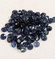 Close-up top and side views of multiple small loose round-cut blue sapphire gemstones showing faceting and color.