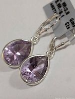 Close-up angled view of two pear-shaped faceted light purple amethyst stones set in polished silver dangle lever-back earrings.