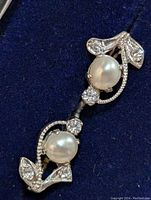 Pair of silver earrings with fresh water pearls and rhinestones on a dark blue fabric background, showing leaf motif design.