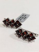 Front angled view of the pair of earrings showing dark red square-cut garnet stones set in sterling silver.