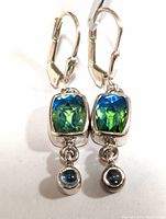 Front view of the silver earrings displaying the green mystic gemstones and blue round accents.
