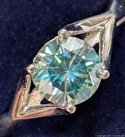 Close-up of the round-cut moissanite gem set in a silver geometric outlined band, showing the gemstone's facets and sparkle.