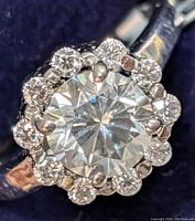 Close-up image of silver ring featuring 2.05 carat round moissanite center stone with halo of smaller round stones surrounding it.