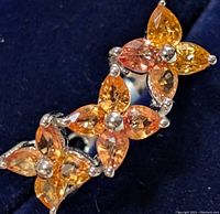 Close-up image of silver ring showcasing clusters of marquise-cut orange sapphire gemstones arranged in floral pattern, highlighting different orange shades and silver prong setting.