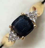 Close-up view of cushion-cut sapphire center stone and white topaz clusters on silver band