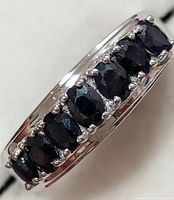 Close-up view of ring showing eight faceted dark blue sapphires set in a polished silver band, viewed from one side.