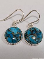 Close-up front view of round turquoise stones set in silver earrings with hook backs