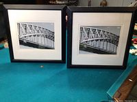 Photo showing two black and white bridge prints side by side on a green surface; each print is in a black wooden frame with white matting and glass front.