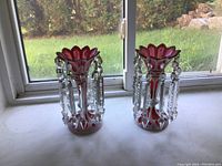 Two cranberry glass lustres side by side on window sill