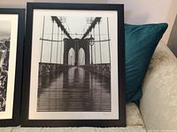 Black and white framed photograph of the Brooklyn Bridge from pedestrian view showing bridge cables and structure.