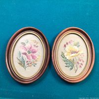 Photo of two oval hand stitched needlework floral pictures in wooden frames.
