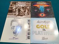 Top view of four vinyl LP album covers arranged in a grid: Alice Cooper Greatest Hits, Boston first album, Mike and the Mechanics, Lynyrd Skynyrd Gold & Platinum.