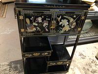Front view of black lacquer cabinet with inlaid birds and flowers on doors and drawer, showing detailed brass door hardware.