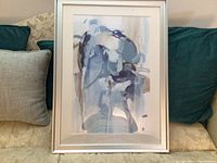 Modern abstract art print framed in silver, showing full artwork and frame against a fabric sofa background.