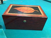Closed wooden box showing the polished finish and leaf inlay design on the lid.