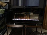 Front view of the electric fireplace with clear crystals illuminated in white with visible flame effect behind the glass panel.