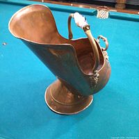 Side view of the copper coal scuttle showing the rounded opening, copper body and ceramic handle with blue decoration.