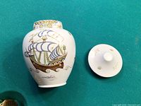 Overall view of white ceramic lidded vase with detailed painting of an old sailing ship. Shows shape, colors, and design of vase and lid.
