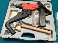 Pneumatic flooring tool in a gray molded plastic case with a black and red nailer, wooden-handled rubber mallet, and a packet of replacement parts