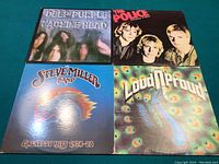 Photo showing four classic rock vinyl LP albums: Deep Purple Machine Head, The Police Outlandos d'Amour, Steve Miller Band Greatest Hits 1974-78, and Nazareth Loud 'N' Proud, arranged on a blue surface.