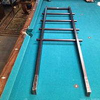Metal Umbra towel ladder lying flat on a pool table showing full length and six horizontal rungs